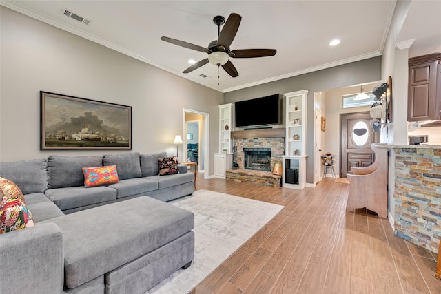 living room featuring ceiling fan, light hardwood / wood-style flooring, crown molding, and a stone fireplace