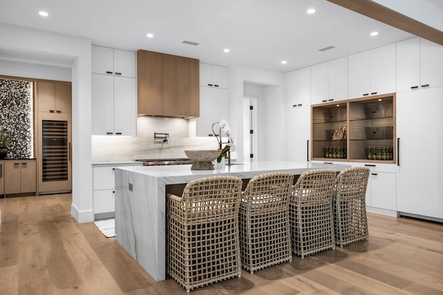 kitchen featuring a kitchen island with sink, white cabinetry, sink, and light hardwood / wood-style floors