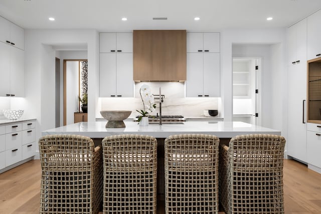 kitchen with a breakfast bar, a kitchen island with sink, white cabinets, and light wood-type flooring