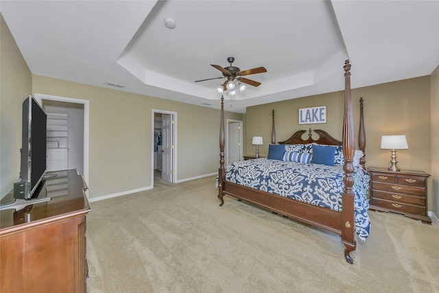 carpeted bedroom with a spacious closet, a closet, ceiling fan, and a raised ceiling