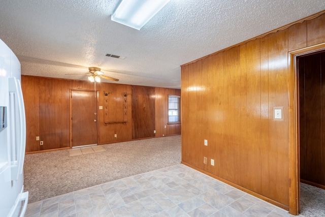 carpeted empty room featuring ceiling fan, wood walls, and a textured ceiling