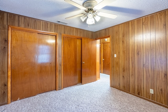 unfurnished bedroom with visible vents, multiple closets, wooden walls, a textured ceiling, and carpet