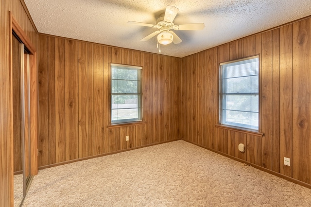 carpeted empty room featuring wood walls, ceiling fan, and a textured ceiling