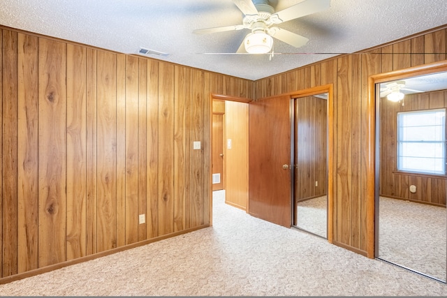 unfurnished bedroom with a textured ceiling, visible vents, a closet, wooden walls, and carpet flooring