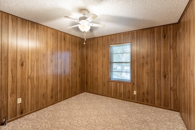 carpeted empty room with a ceiling fan, wood walls, and a textured ceiling