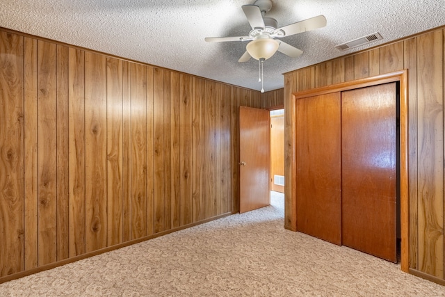 unfurnished bedroom with a textured ceiling, wooden walls, a closet, ceiling fan, and light carpet