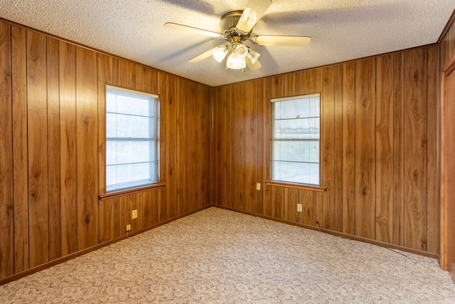 carpeted empty room with ceiling fan, a wealth of natural light, a textured ceiling, and wood walls