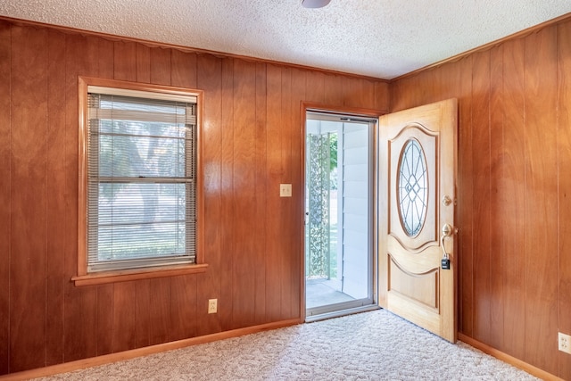 entrance foyer featuring a textured ceiling, carpet flooring, and wooden walls