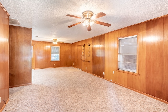 empty room with ceiling fan, wood walls, a textured ceiling, and light colored carpet