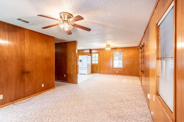 spare room featuring wooden walls, light colored carpet, a textured ceiling, a ceiling fan, and visible vents