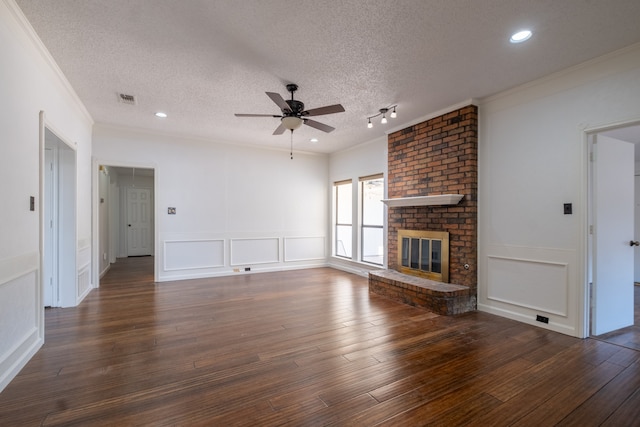 unfurnished living room with ceiling fan, dark wood-type flooring, rail lighting, a fireplace, and a textured ceiling