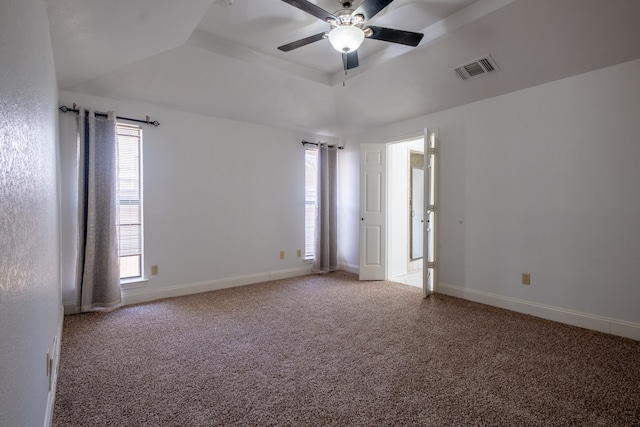 carpeted empty room with a wealth of natural light, ceiling fan, and a raised ceiling