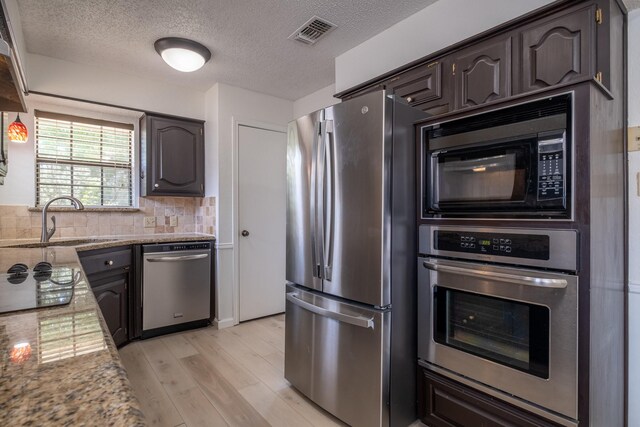 kitchen featuring appliances with stainless steel finishes, light hardwood / wood-style flooring, backsplash, dark brown cabinetry, and light stone counters