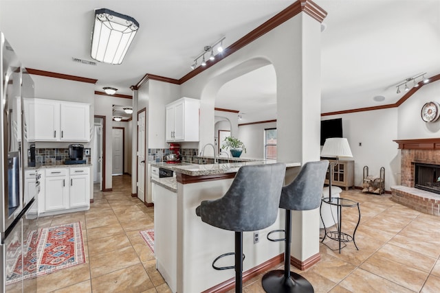 kitchen featuring backsplash, a brick fireplace, ornamental molding, light tile patterned floors, and kitchen peninsula