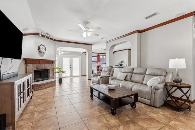 tiled living room with ceiling fan, crown molding, and a brick fireplace