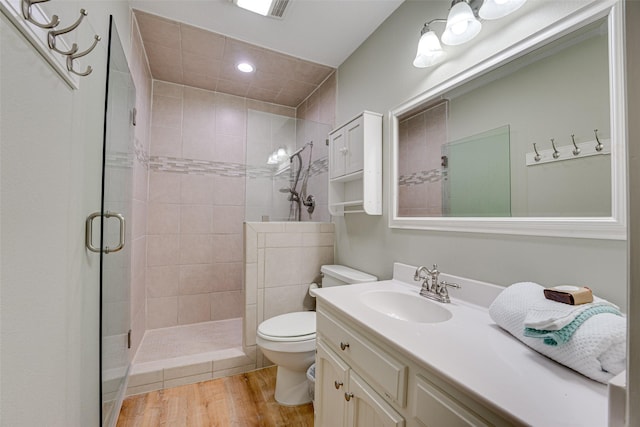 bathroom with a tile shower, hardwood / wood-style floors, vanity, and toilet