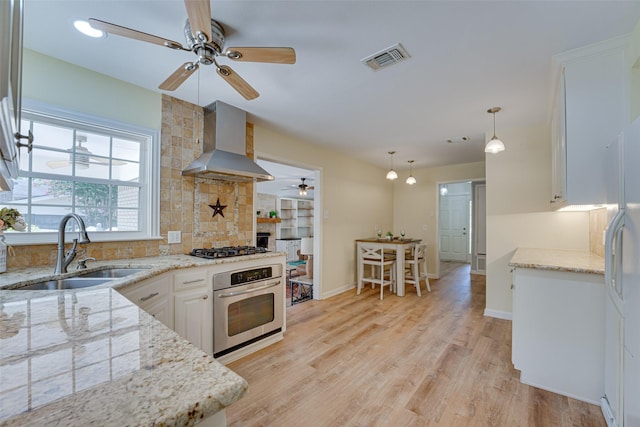 kitchen with appliances with stainless steel finishes, sink, wall chimney range hood, decorative light fixtures, and white cabinetry