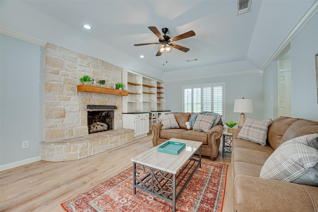 living room with ceiling fan, a stone fireplace, light wood-type flooring, and crown molding