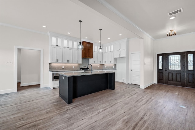 kitchen featuring light hardwood / wood-style flooring, white cabinetry, light stone counters, a center island with sink, and pendant lighting