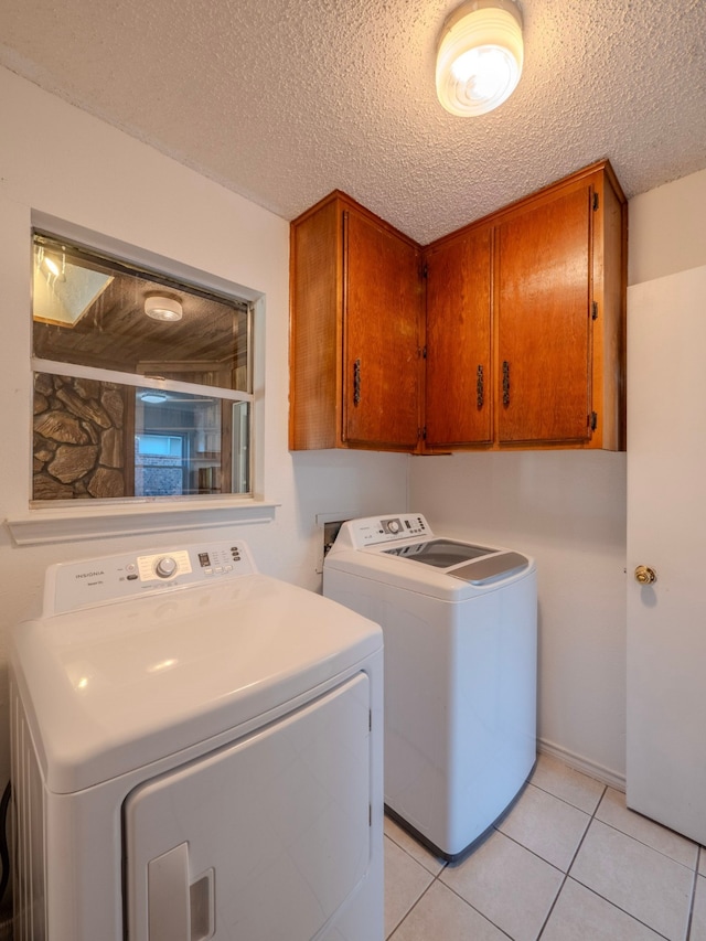 clothes washing area with washer and clothes dryer, cabinets, a textured ceiling, and light tile patterned flooring