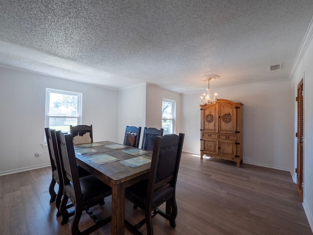 dining space with dark wood-type flooring, a textured ceiling, an inviting chandelier, and ornamental molding