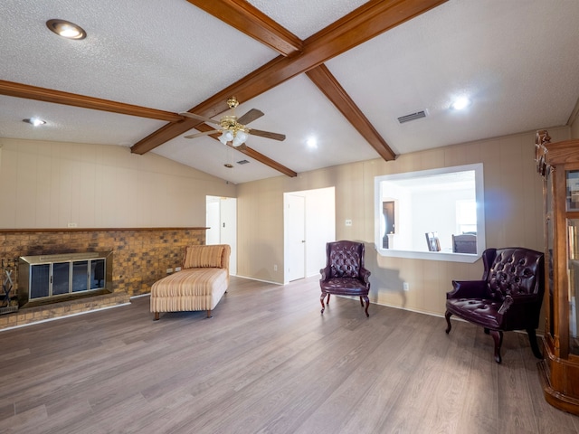 living area featuring wood-type flooring, vaulted ceiling with beams, a fireplace, a textured ceiling, and ceiling fan