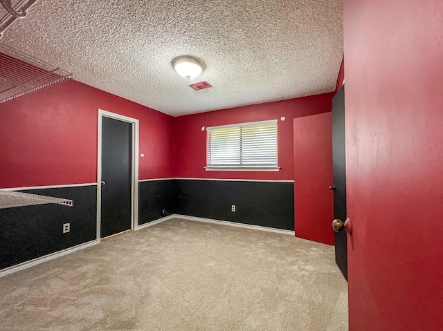 unfurnished bedroom featuring a textured ceiling, carpet, visible vents, and baseboards