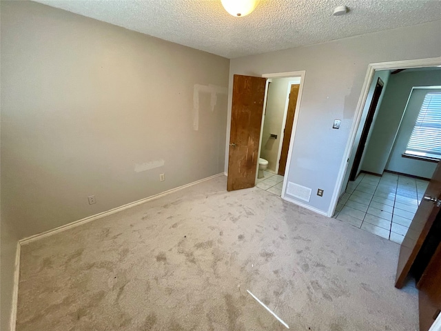 unfurnished bedroom with ensuite bathroom, a textured ceiling, and light carpet