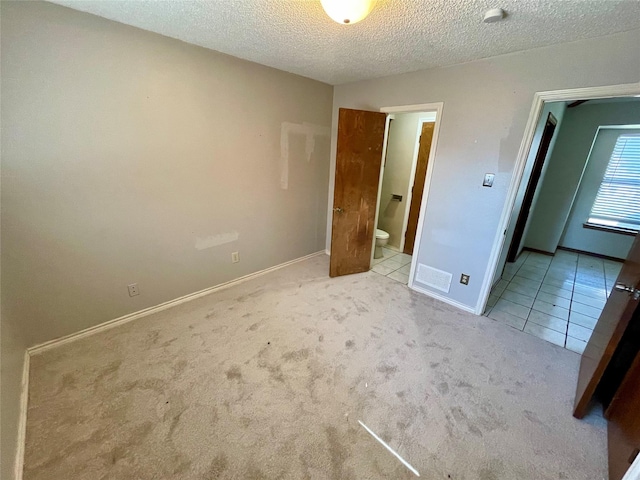 unfurnished bedroom featuring a textured ceiling, baseboards, tile patterned floors, carpet, and ensuite bath