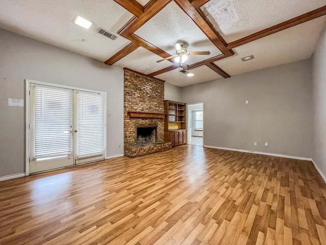 unfurnished living room featuring light wood-type flooring, a textured ceiling, and a brick fireplace