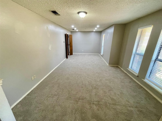 spare room with carpet floors, a wealth of natural light, a textured ceiling, and baseboards