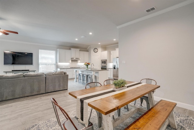 dining space featuring ceiling fan, ornamental molding, sink, and light hardwood / wood-style flooring