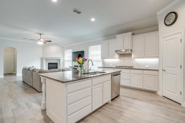 kitchen featuring dark stone counters, stainless steel appliances, sink, white cabinets, and an island with sink