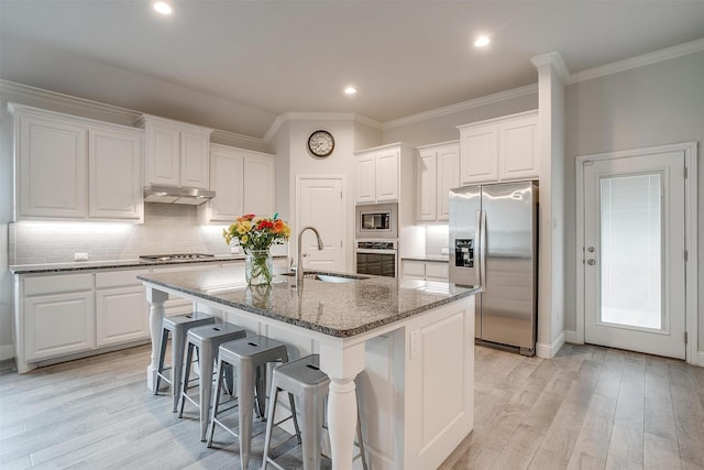 kitchen featuring sink, appliances with stainless steel finishes, a kitchen island with sink, white cabinetry, and dark stone countertops