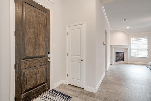 entryway with crown molding, a brick fireplace, and light wood-type flooring