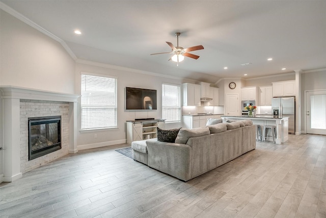 living room with crown molding, a fireplace, light hardwood / wood-style floors, and ceiling fan