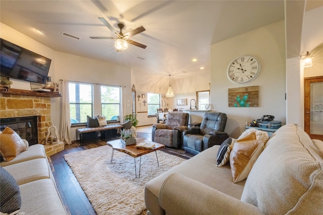 living room with ceiling fan, dark hardwood / wood-style floors, and a stone fireplace