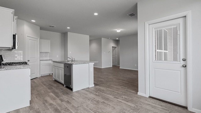 kitchen featuring backsplash, appliances with stainless steel finishes, light wood-type flooring, a kitchen island with sink, and white cabinets