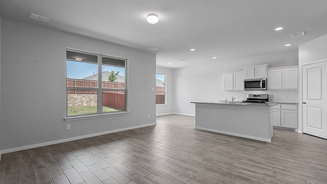 kitchen with backsplash, light wood-type flooring, a kitchen island with sink, white cabinetry, and stainless steel appliances