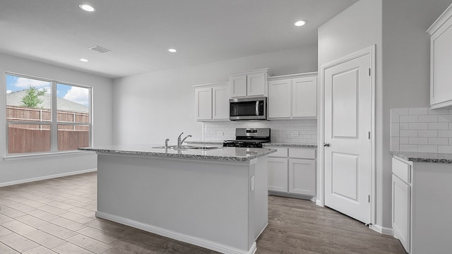 kitchen featuring appliances with stainless steel finishes, an island with sink, and white cabinets