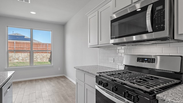 kitchen featuring light stone countertops, light hardwood / wood-style floors, tasteful backsplash, stainless steel appliances, and white cabinets