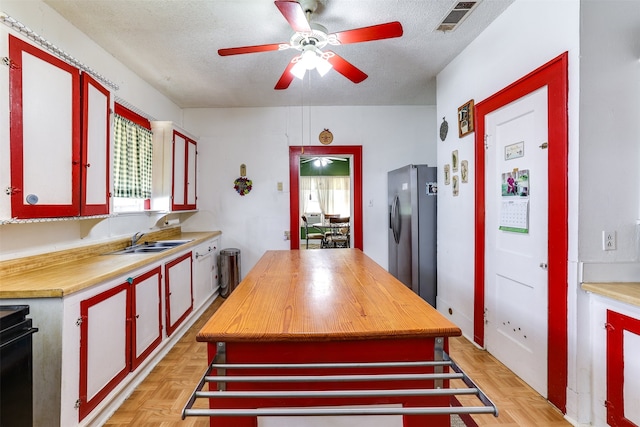 kitchen featuring stainless steel refrigerator with ice dispenser, visible vents, a sink, wood counters, and a textured ceiling