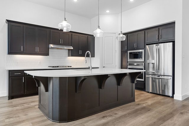 kitchen with appliances with stainless steel finishes, light hardwood / wood-style flooring, a center island with sink, and decorative backsplash