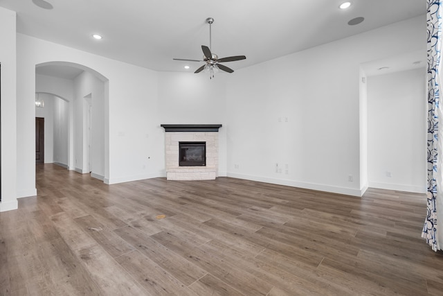 unfurnished living room with ceiling fan, a fireplace, and wood-type flooring