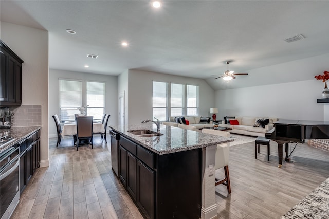 kitchen with light hardwood / wood-style floors, light stone countertops, an island with sink, and ceiling fan