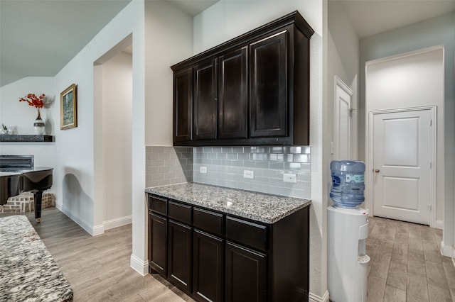 kitchen featuring dark brown cabinetry, light stone countertops, light wood-type flooring, and decorative backsplash