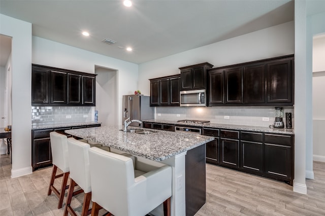 kitchen with light hardwood / wood-style floors, appliances with stainless steel finishes, a breakfast bar area, and an island with sink