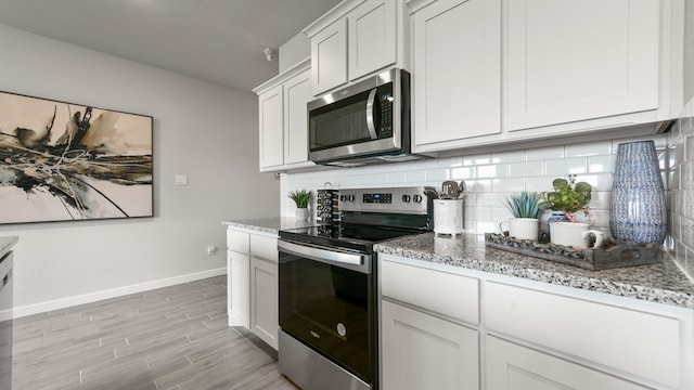 kitchen featuring white cabinets, decorative backsplash, appliances with stainless steel finishes, and light stone counters