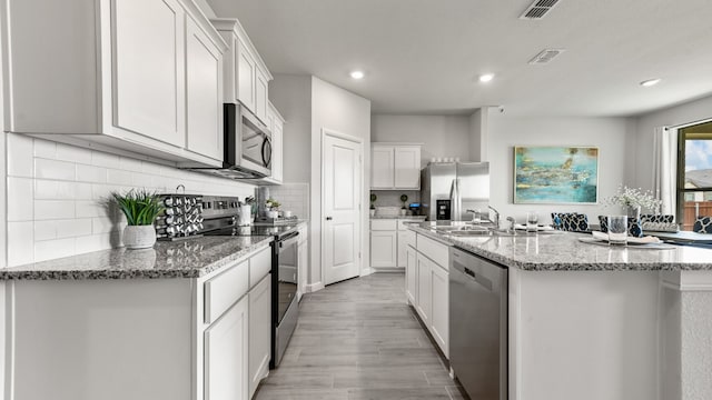 kitchen featuring stainless steel appliances, white cabinets, and an island with sink