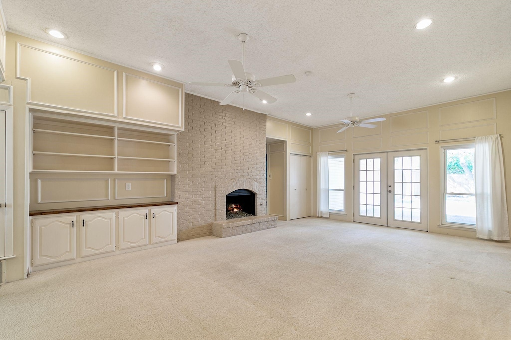 unfurnished living room featuring a textured ceiling, ceiling fan, light colored carpet, and a fireplace